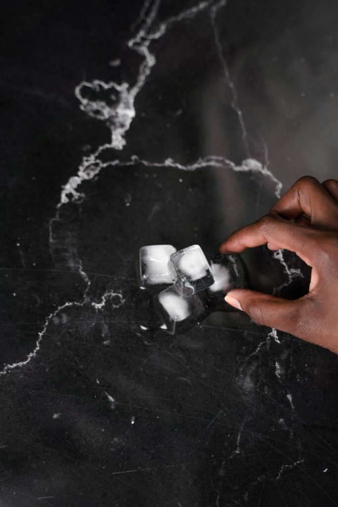 Close-up of a hand touching ice cubes on a black marble surface, showing texture and contrast.