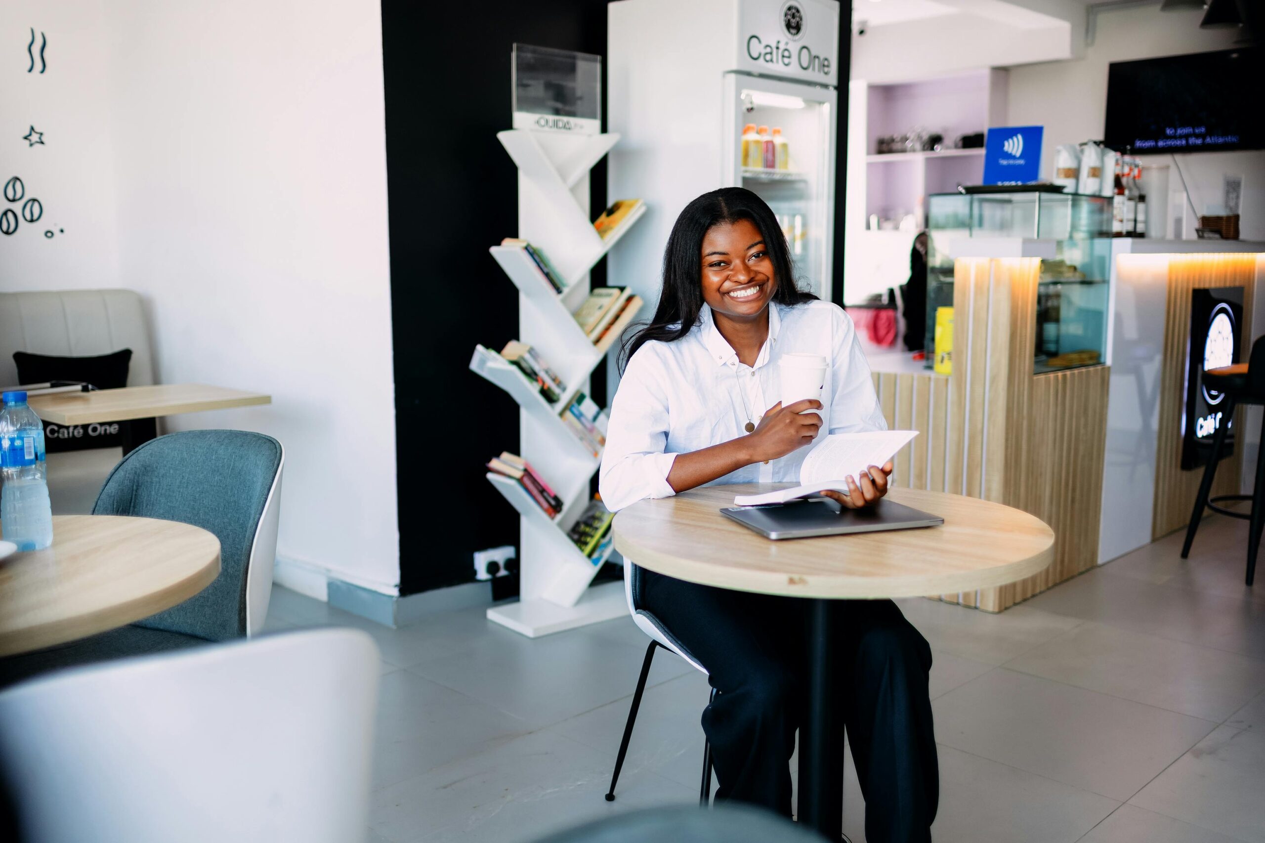 Smiling woman enjoys a book and coffee in a modern Lagos café.